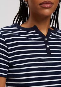 Niebiesko-biała koszula z krótkim rękawem w paski, z okrągłym dekoltem i zapięciem na dwa guziki. Ribbowany materiał, luźny krój.