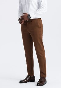 Braune Hosen mit schlanker Passform, flacher Vorderseite, zwei Seitentaschen und glatter Textur, kombiniert mit dunkelbraunen Business-Schuhen.