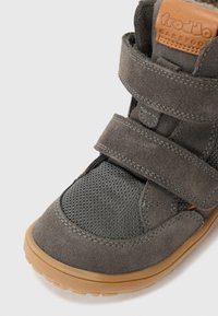 Gray suede shoe with mesh accents, double Velcro straps, and a brown leather label. Rubber sole with textured grip for stability.