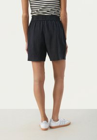 Shorts en lin bleu marine avec taille élastique, coupe longueur genou, et poches latérales, associés à des chaussures de sport blanches.