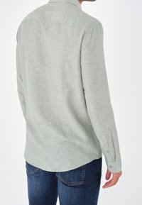 Camisa de manga larga verde claro hecha de una tela texturizada, con cuello y puños abotonados, combinada con unos jeans de mezclilla azul oscuro.