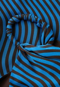 Tissu rayé bleu et marron torsadé en boucle et posé sur un fond en tissu rayé assorti.