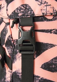 Primo piano di una borsa a motivo rosa e nero con una fibbia di plastica nera e cinghie, realizzata in tessuto testurizzato che mostra un design grafico.