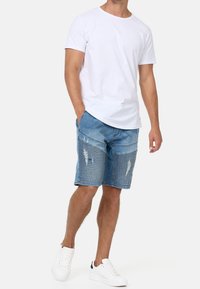 T-shirt en coton blanc et short en denim bleu avec des détails déchirés et un motif à rayures horizontales, associés à des baskets blanches.