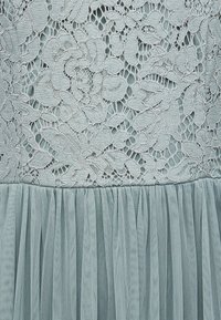 Λεπτό γαλάζιο ύφασμα με φλοράλ δαντέλα στην κορυφή και διάφανο, πλισέ διχτυωτό υλικό από κάτω.