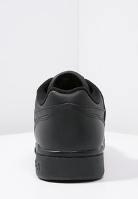 Černé kožené tenisky s texturovaným povrchem, polstrovaným límcem a minimalistickým designem. Obsahují gumovou podrážku s decentním logem.