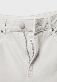 Bela jeans iz denima z zadrgo spredaj, srebrnim gumbom za zapiranje in oznako "BODI SVOJA MUZA". Imajo kontrastne roza šive.