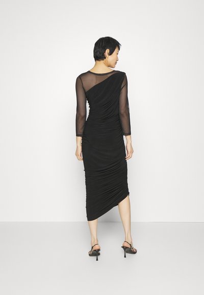 Czarna sukienka z dopasowanej, teksturowanej tkaniny, z marszczeniami, długimi przezroczystymi rękawami i ukośnym dołem z tyłu.