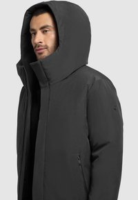 Black puffer jacket with a high collar and large hood. Features side zip pockets and a sleek, smooth texture. Minimalist design.