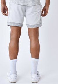 Shorts de sport gris avec une taille élastique, présentant un ourlet à motifs et des accents de logo. Portés avec des chaussettes blanches et des baskets.