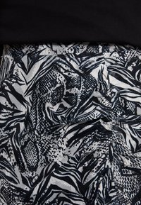 Tessuto in bianco e nero con motivi astratti che combinano strisce e texture. La superficie stropicciata aggiunge profondità al design.