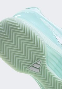 Semelle de chaussure de sport bleu clair avec motif en chevrons et petit logo triangulaire réfléchissant près de la zone des orteils.