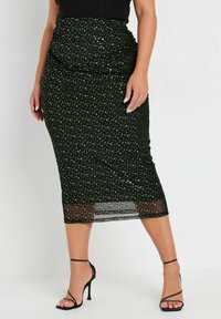 Czarna spódnica midi w białe kropki, marszczony fason w talii, przezroczysty dół, zestawiona z czarnymi sandałami na wysokim obcasie.