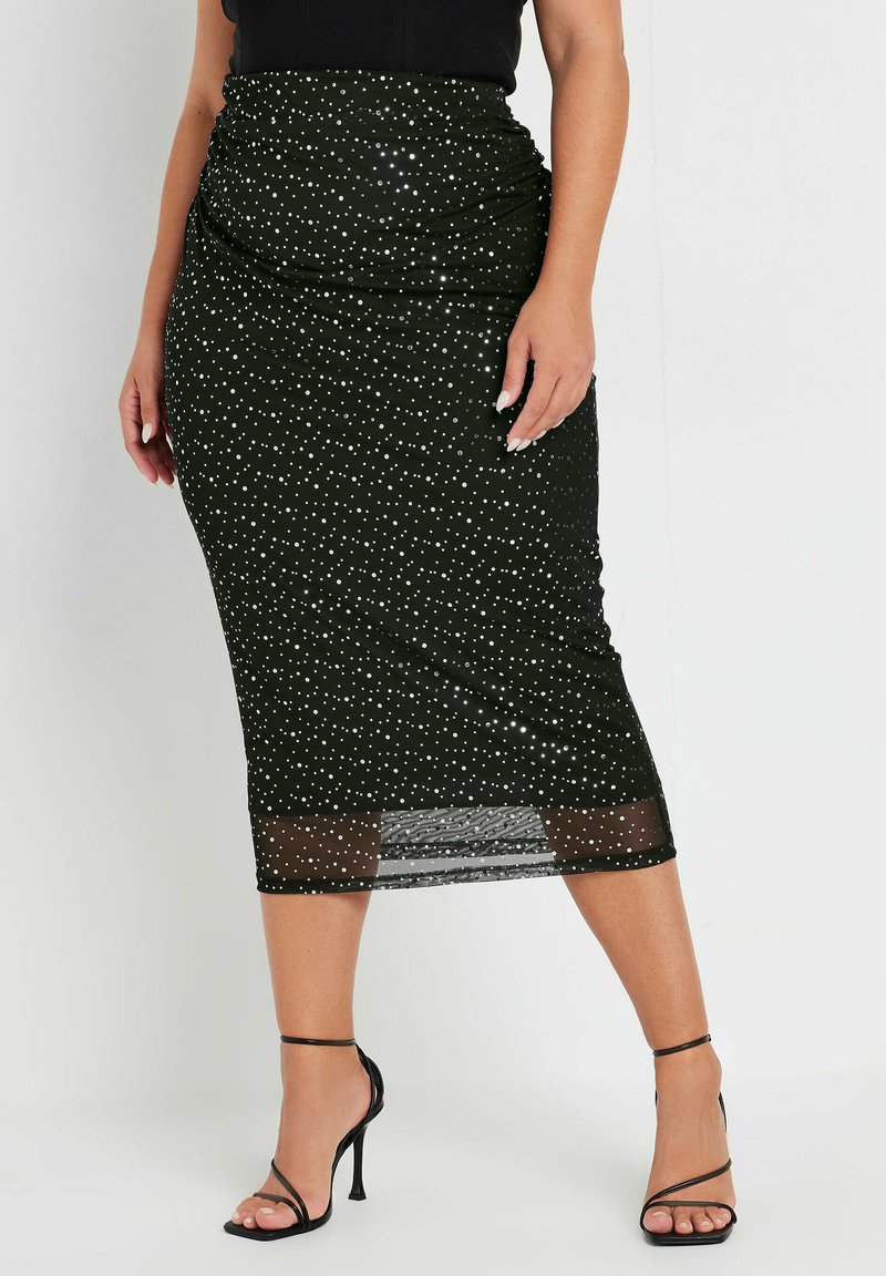 Czarna spódnica midi w białe kropki, marszczony fason w talii, przezroczysty dół, zestawiona z czarnymi sandałami na wysokim obcasie.