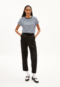 Gestreept T-shirt in marineblauw en wit, korte mouwen, gecombineerd met hoge zwarte broeken. Model draagt zwart-witte loafers met witte sokken.