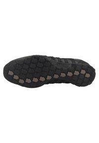 Semelle de chaussure de sport noire présentant une texture en caoutchouc avec des motifs circulaires, offrant adhérence et durabilité. Accents dans une teinte plus claire.