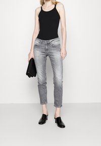 Top negro sin mangas combinado con jeans ajustados gris claro, con ligero desgaste, y mule con tacón negro. Clutch negro bajo el brazo.