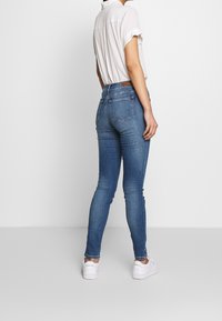 Dunne blauwe denim jeans met een hoge taille, met achterzakken en een nauwsluitende pasvorm langs de benen. Gecombineerd met witte sneakers.