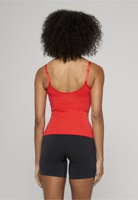 Rød tanktop med justerbare stropper parret med sorte shorts. Stoffet virker glatt og tettsittende, designet for komfort og bevegelse.