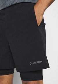 Shorts sportivi neri da uomo con tasche laterali, realizzati in tessuto morbido, con un accento di logo e un interno aderente.