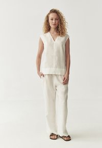Linen top un platām kājām biksēm off-white krāsā. Topam ir V-veida kakla izgriezums un īsas piedurknes. Sandales ar tumšiem siksniņām. Gluda, viegla auduma.