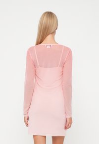 Šviesiai rožinė ilgomis rankovėmis suknelė, pagaminta iš permatomos medžiagos, su apvaliu iškirpimu ir prigludusiu siluetu, matomomis siūlių detalėmis ant nugaros.