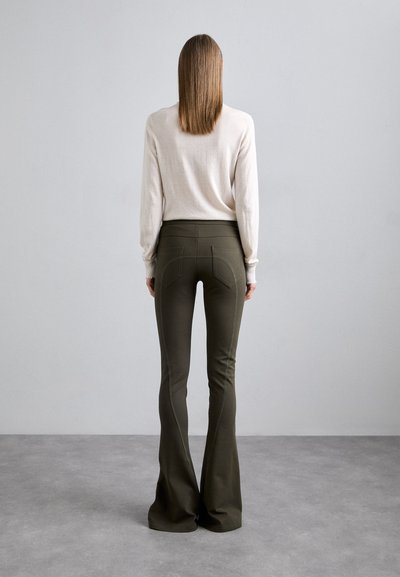 Olijfgroene flared broek met een hoge taille, voorzien van gestructureerde zakken aan de achterkant en zichtbare stiksels. Gecombineerd met een lichtbeige lange mouwtop.
