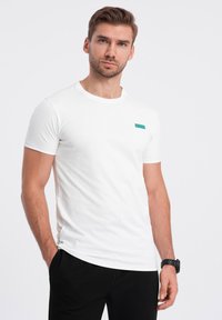 Bílý bavlněný tričko s kulatým výstřihem, které má malé tyrkysové logo na levé části hrudi a je navrženo v slim fit střihu.