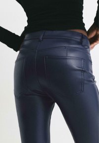 Granatowe spodnie z ekoskóry cechują się dopasowanym krojem, kieszeniami oraz gładką fakturą, podkreślone wysokim stanem i minimalnym szwem.