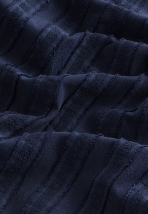 Tengerészkék szövet hullámos csíkokkal, változó textúrával, puha, sima felülettel és foszló élekkel, dinamikus vizuális hatást keltve.