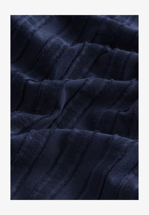 Tengerészkék szövet hullámos csíkokkal, változó textúrával, puha, sima felülettel és foszló élekkel, dinamikus vizuális hatást keltve.