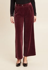 Pantaloni in corda bordeaux a gamba larga con pieghe, dotati di chiusura con bottone e tessuto testurizzato, abbinati a scarpe nere.