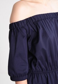 Dunkelblaues Off-Shoulder-Kleid mit elastischem Ausschnitt und Puffärmeln. Glatter, leichter Stoff mit gerafftem Bund für eine lockere Passform.