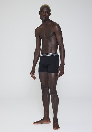Sorte boxer shorts med en tætsiddende design og en hvidstribet talje, vist på en mandlig model. Glat stoftekstur, kort længde.