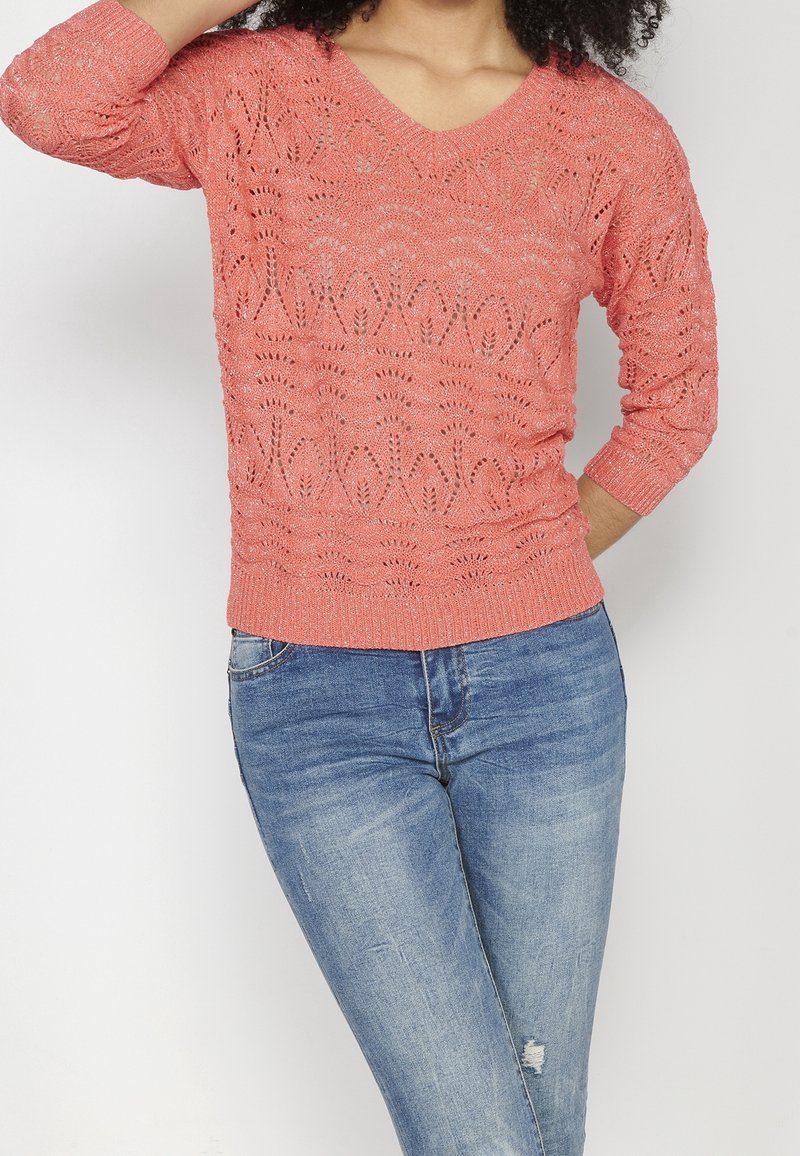 Pull en maille corail avec col en V, manches trois-quarts et motif texturé. Associé à un jean en denim bleu.