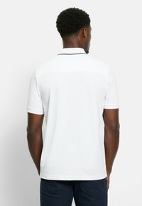 Weißes Poloshirt mit kurzen Ärmeln und Kragen, mit kontrastierendem Besatz. Glattes, atmungsaktives Material. Einfaches und sauberes Design.