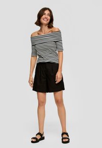 Zwarte linnen shorts gecombineerd met een zwart-wit gestreepte off-the-shoulder top. De schoenen hebben chunky zwarte geweven banden.
