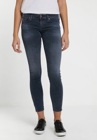 Smala jeans i mörkblå denim, med medelhög midja, fem fickor och subtila blekningar. Matchas med svarta sneakers för en avslappnad look.
