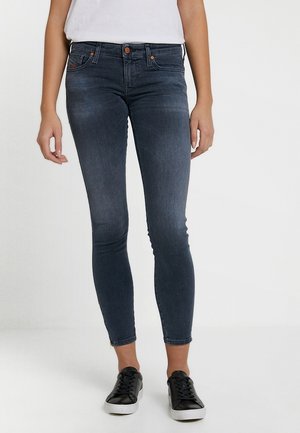 Jeans ajustados en denim azul oscuro, con una cintura de altura media, cinco bolsillos y un ligero desvanecimiento. Combinados con zapatillas negras para un look casual.