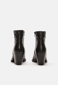 Bottines en cuir noir avec une finition lisse, dotées d'une fermeture éclair et de talons empilés, affichant un design élégant et structuré.