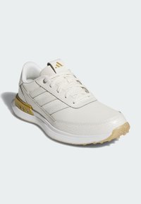 White athletic shoes featuring a textured upper, three striped accents, and a gold heel piece, with a semi-transparent outsole.