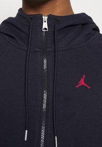 Ciemnoniebieska bluza z zamkiem, wykonana z miękkiego materiału, z czerwonym logo Jordana na klatce piersiowej i srebrnymi zamkami.