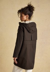 Parka imperméable marron avec une capuche bordée de fourrure, des cordons ajustables et des poches à rabat. Présente une coupe décontractée et une longueur mi-cuisse.