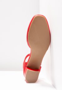 Chaussure à talons hauts rouge avec une tige en cuir lisse, un bout effilé et une semelle en caoutchouc beige texturée. Aucune décoration ni motif visible.