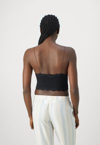 Bralette preto com renda, al�ças ajustáveis, design justo e textura suave, combinado com calças riscadas de cor clara.