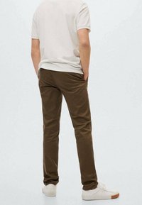 Hnědé slim-fit kalhoty s hladkým povrchem, které jsou kombinovány se světle šedým tričkem. Bílí tenisky se světlými hnědými podešvami dotvářejí celkový vzhled.