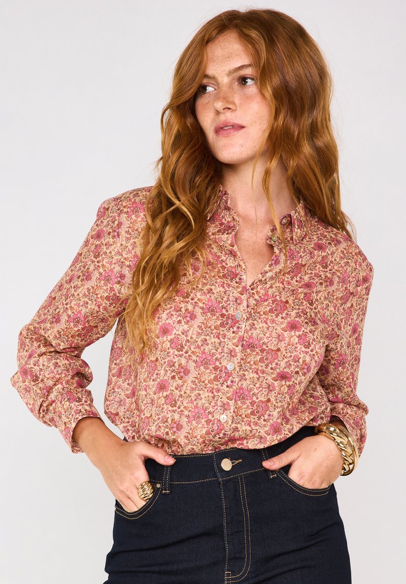 Chemise à boutons à motif floral en tissu rose et crème, avec manches longues, col à revers et coupe décontractée. Associée à un jean en denim foncé.