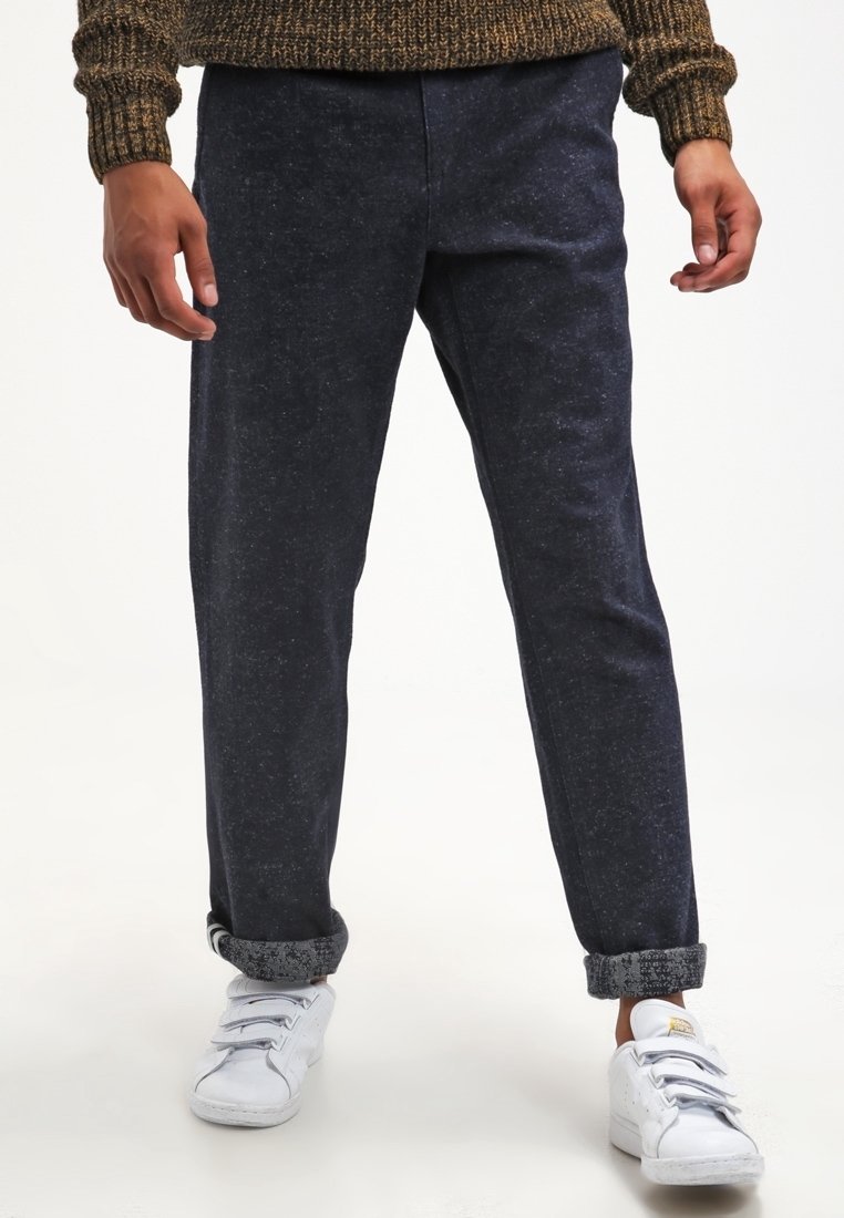 Dark blue relaxed-fit pants made of textured fabric, featuring rolled cuffs and complemented by white sneakers. No visible patterns or accents.