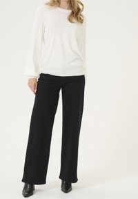 Vit stickad tröja med strukturerade puffärmar, kombinerad med vida svarta jeans och svarta ankelskor. En enkel och modern design.