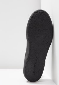 Semelle en caoutchouc noir d'une chaussure avec une adhérence texturée et le nom de la marque Superga embossé au centre en bas.